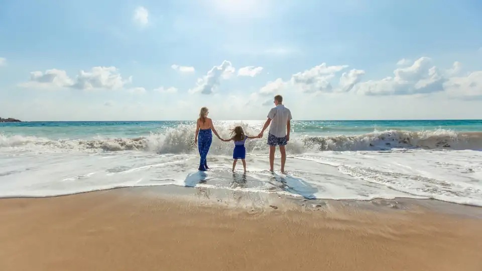 Parents and child standing together at the ocean's edge, looking toward the waves